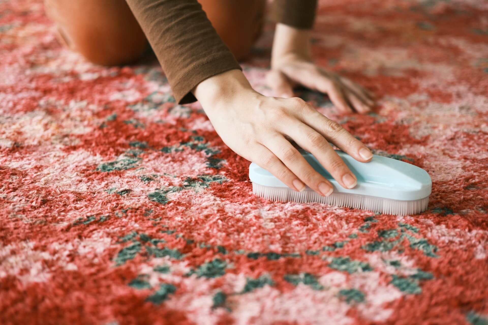 A woman cleans a red carpet using a white brush